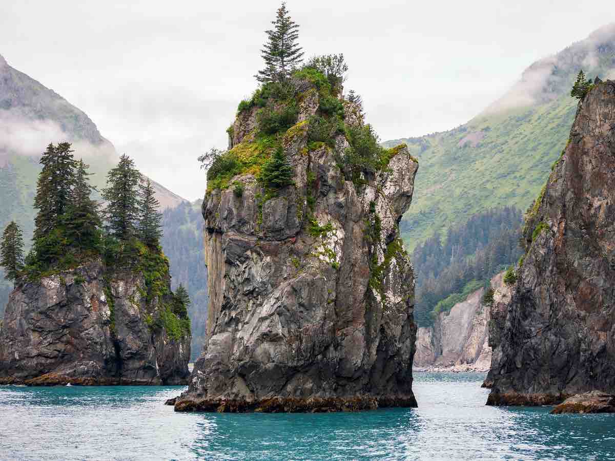 stacks of rock formations with tree foliage on waters in alaska